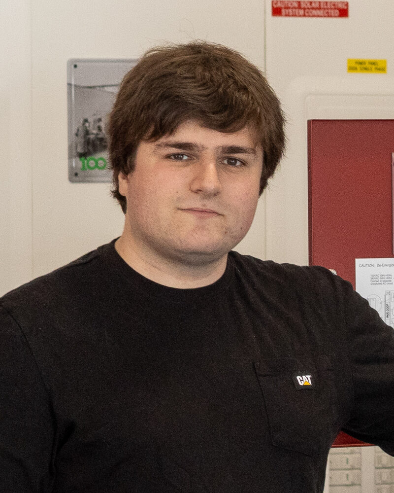 Sam Zimmerman in a black sweater, standing beside a fire alarm panel